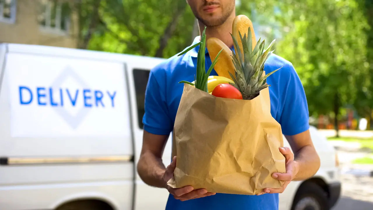 Grocery delivery driver holding a paper bag filled with fresh produce outside a delivery van, promoting El Gran Valle Verde’s grocery delivery service in Hamilton, Ohio.