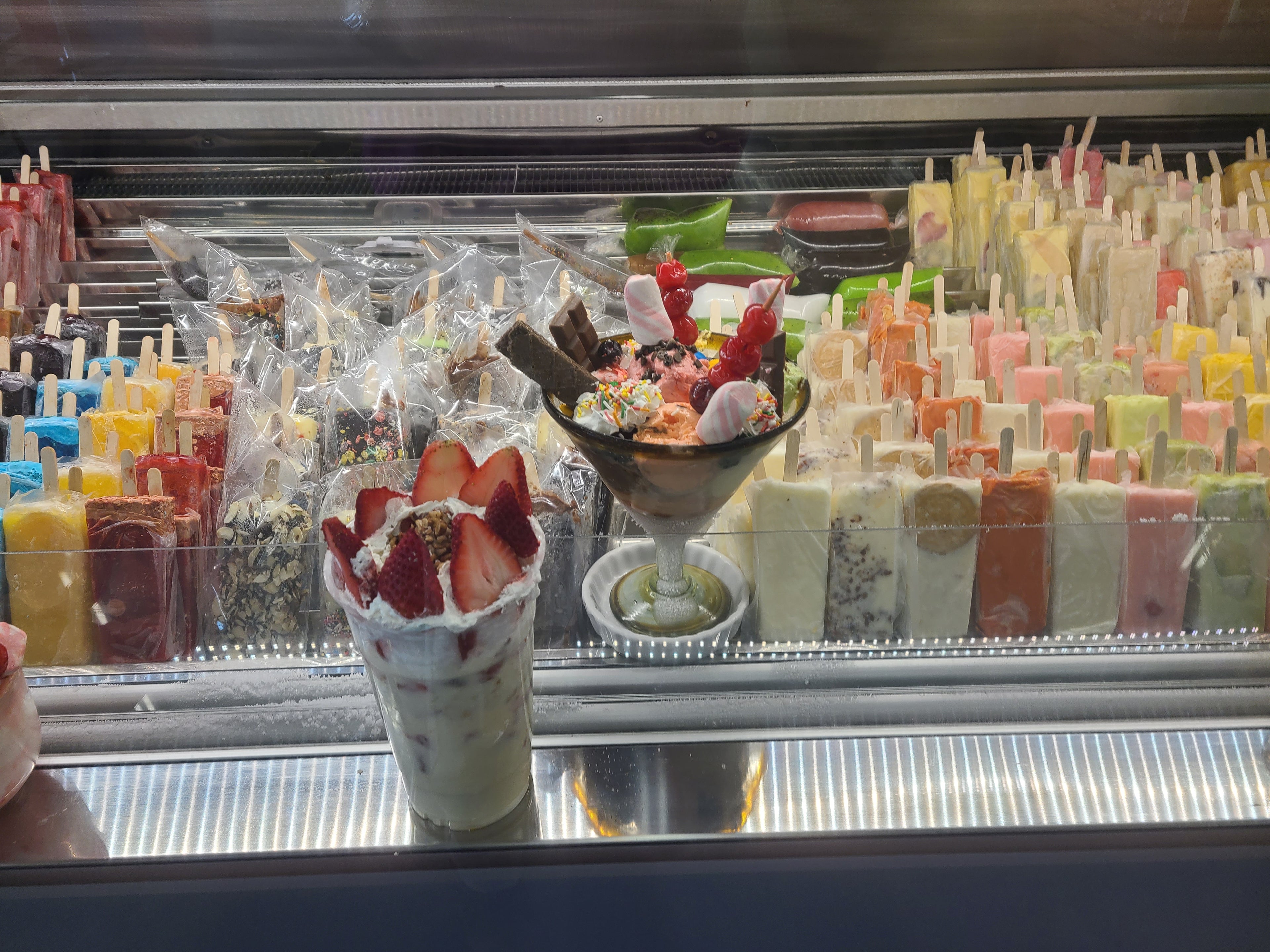 Display case filled with colorful Mexican ice creams, paletas, and specialty desserts at the Heladería inside El Gran Valle Verde, a Hispanic grocery store in Hamilton, Ohio.