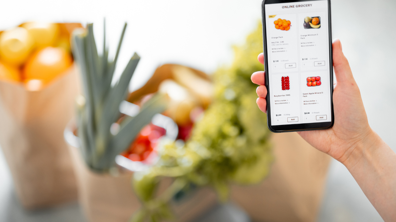 A customer uses a smartphone to order fresh groceries online from El Gran Valle Verde in Hamilton, Ohio, with bags of produce in the background, promoting convenient grocery shopping on your schedule.